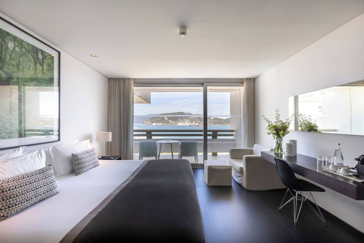 Un hotel moderno con una cama grande, un escritorio, una silla y vista al mar.