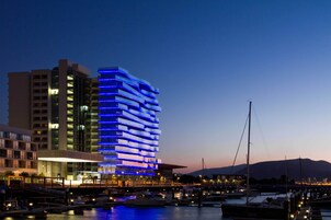 Un hotel moderno con una fachada iluminada en azul, situado cerca de un puerto deportivo con barcos amarrados.