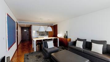 A modern living room with a sofa, ottoman, and a dining area with a kitchen in the background.