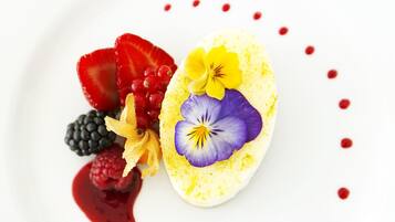 A white plate with a dessert featuring a yellow base, purple and yellow flowers, and red berries.