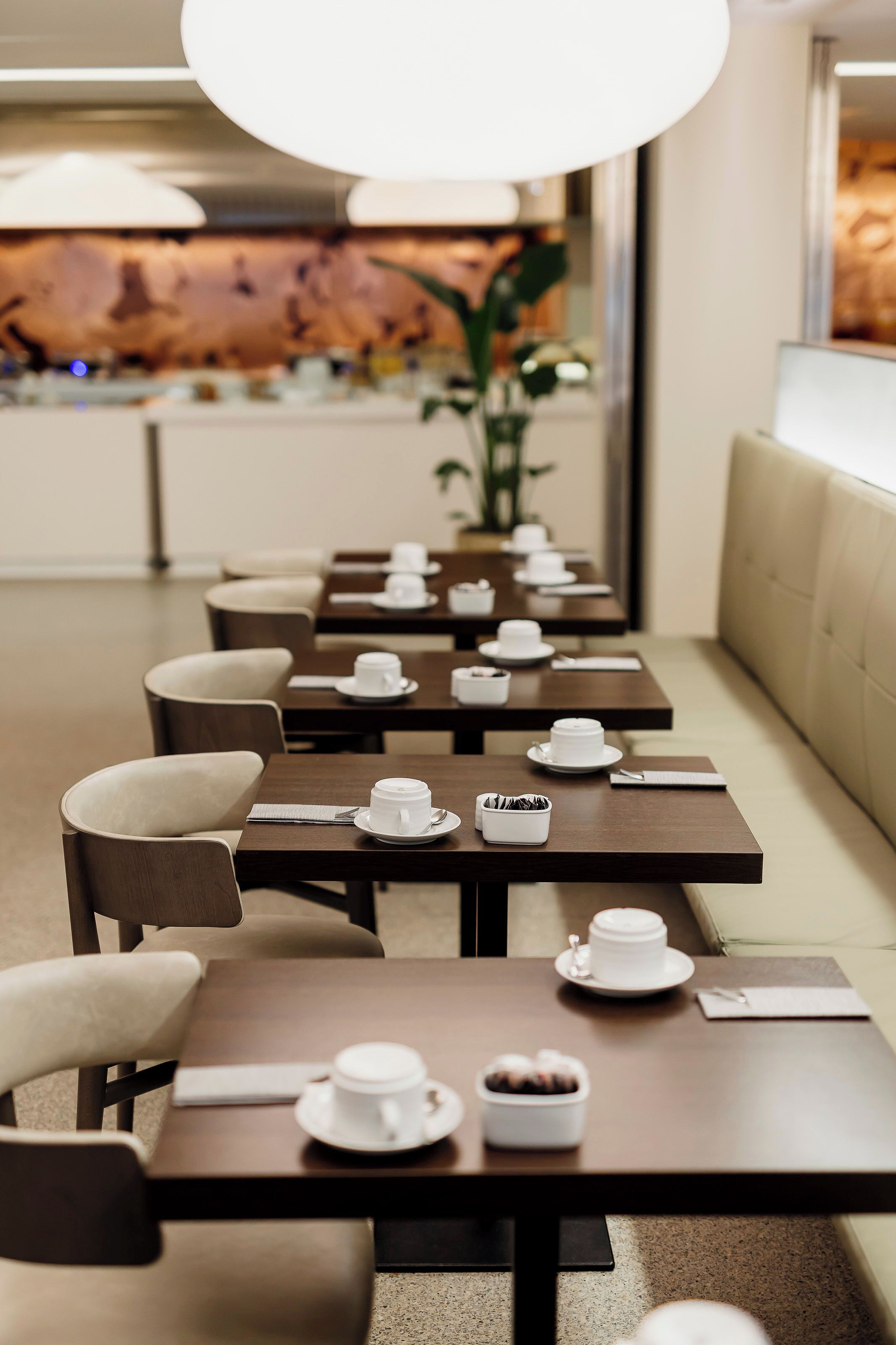 A restaurant with multiple tables, each set with white cups and saucers, and a few with small bowls of food.