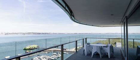Un balcon doté d’une balustrade en verre, donnant sur une marina où sont amarrés des bateaux et un ferry.