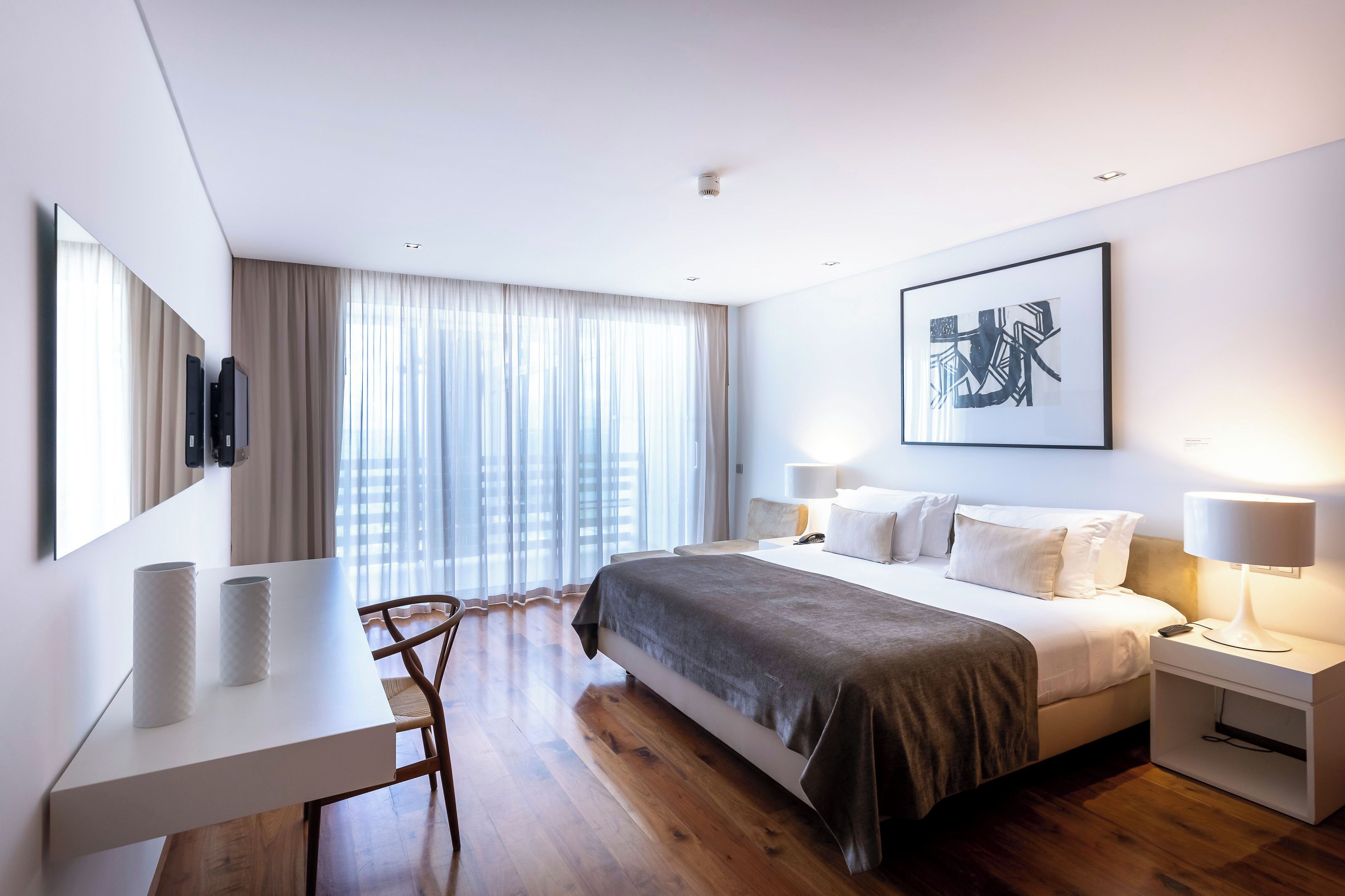 Una habitación de hotel moderna con una cama grande, mesitas de noche, un escritorio y una silla.