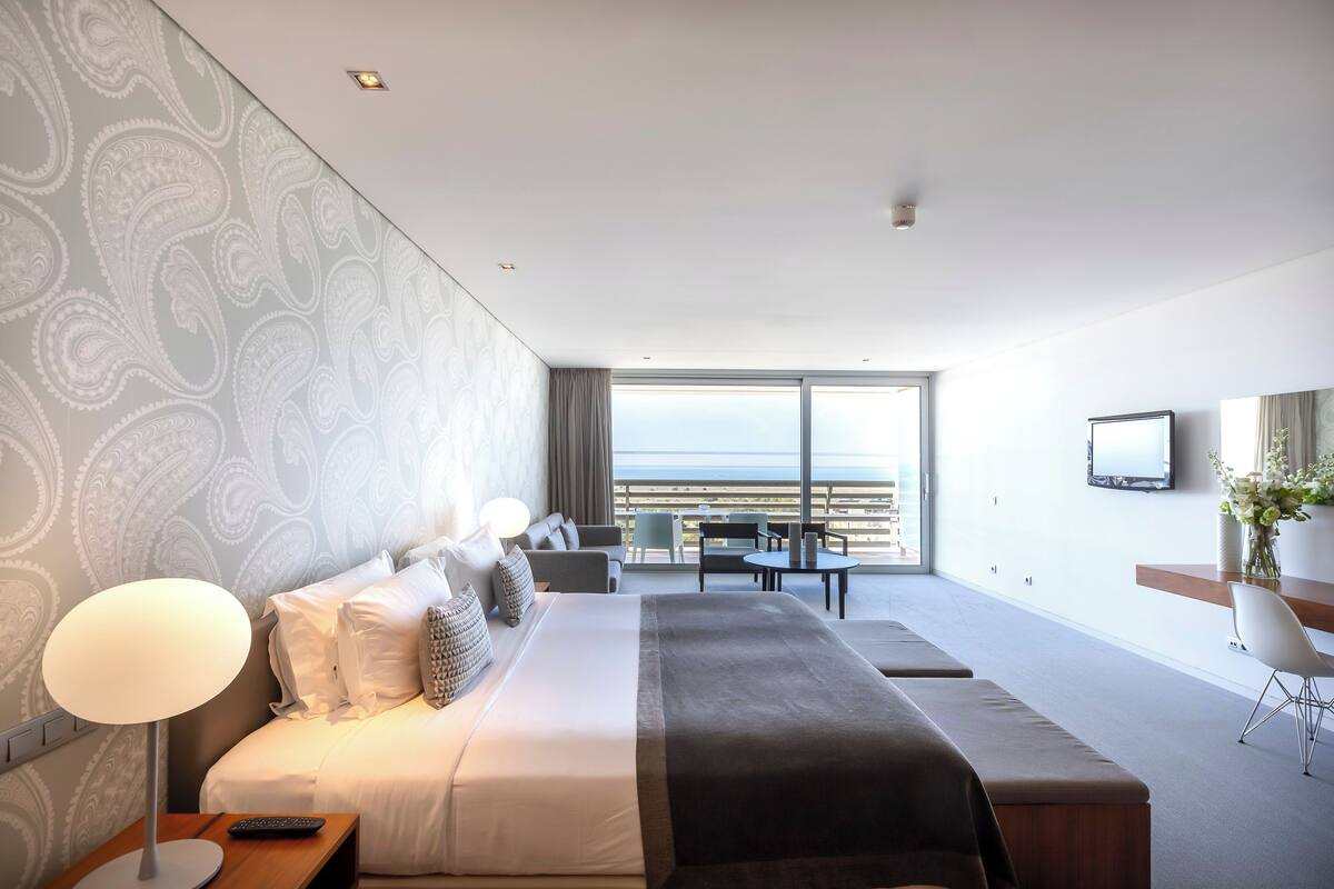 Una habitación de hotel moderna con una cama grande, un escritorio y un balcón con vistas al mar.