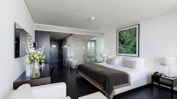 Una habitación de hotel moderna con una cama grande, una mesita de noche con lámpara, un baño con bañera y un amplio ventanal.