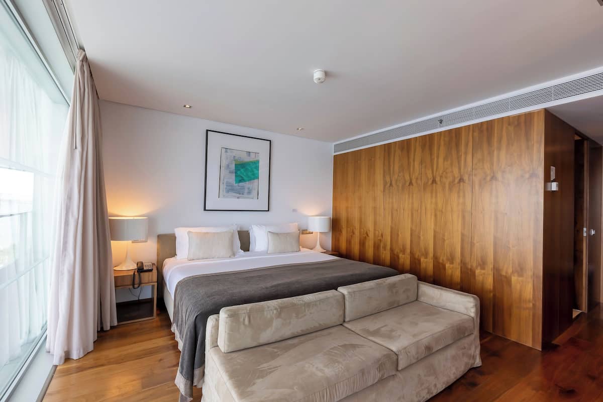 Una habitación de hotel moderna con una cama grande, lámparas de noche, un armario de madera y una ventana con cortinas.