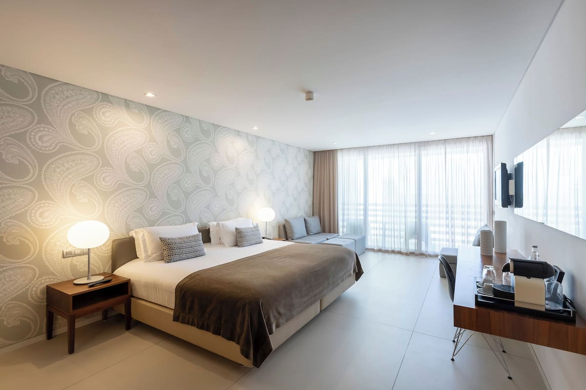 Una habitación de hotel moderna con una cama grande, mesitas de noche, un escritorio y un televisor montado en la pared.