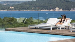 Un área junto a la piscina con sillones de descanso y vistas al mar y las colinas.