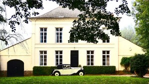 A two-story building with a symmetrical facade, a central entrance, and a classic car parked in front. - Maison de Plumes (Heuchin)