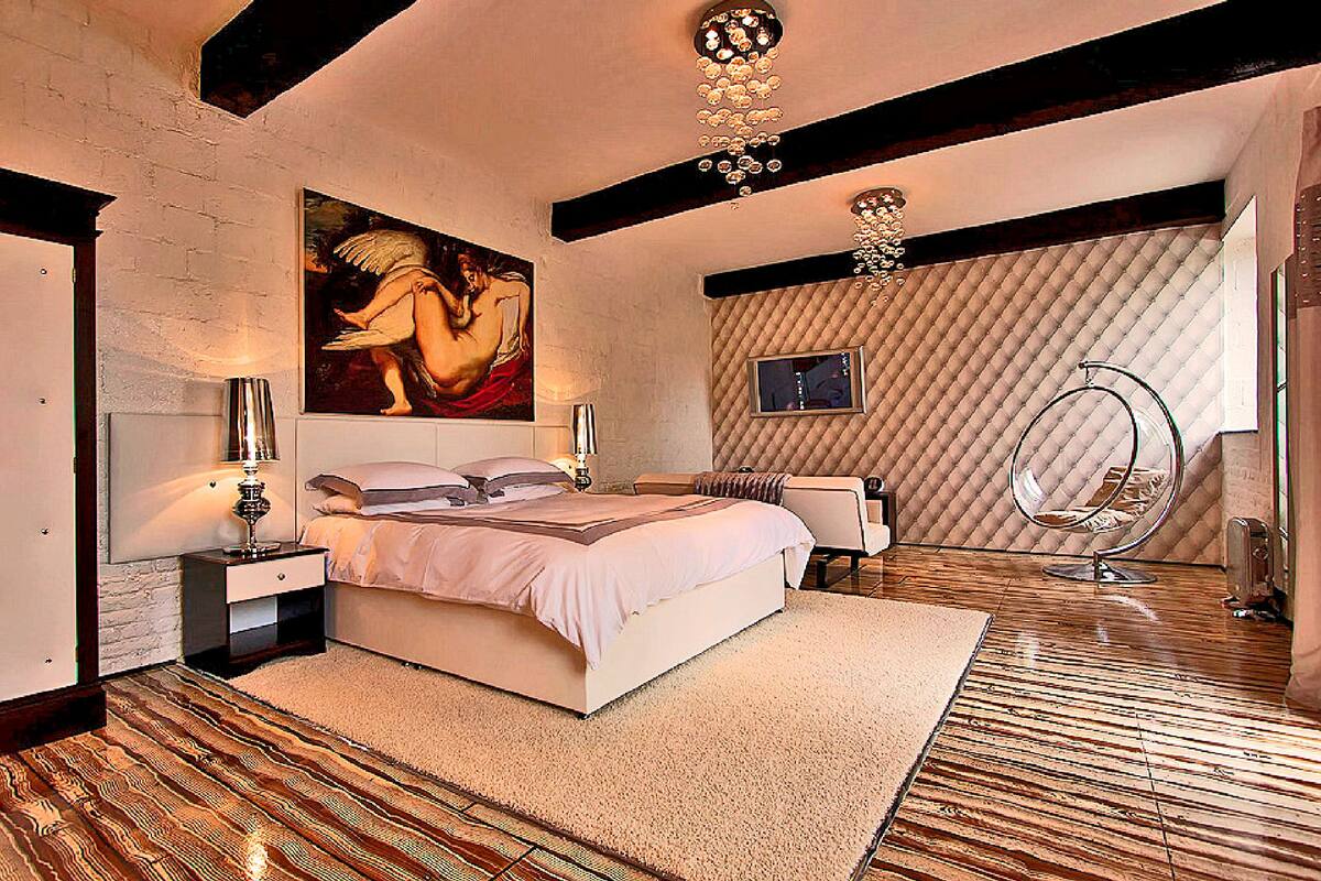 A bedroom with a large bed, a painting, a television, and a unique circular chair.