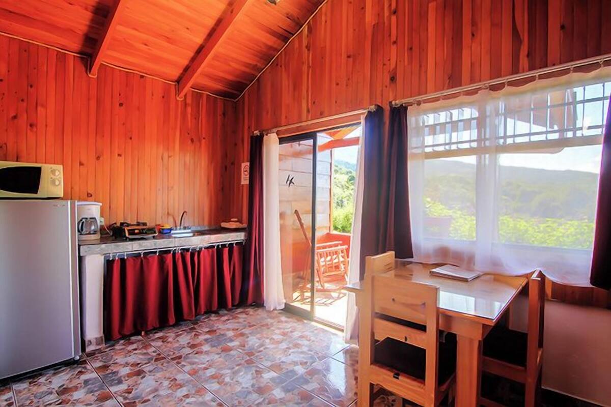 A wooden interior with a kitchen, a dining table, and a view through a glass door.