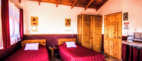 A room with two beds, wooden ceiling beams, a wardrobe, and a small table with a kettle.