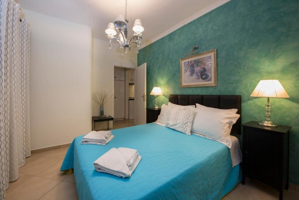 Une chambre à coucher avec une couvre-lit bleue, des oreillers blancs, un lustre et deux lampes de chevet.