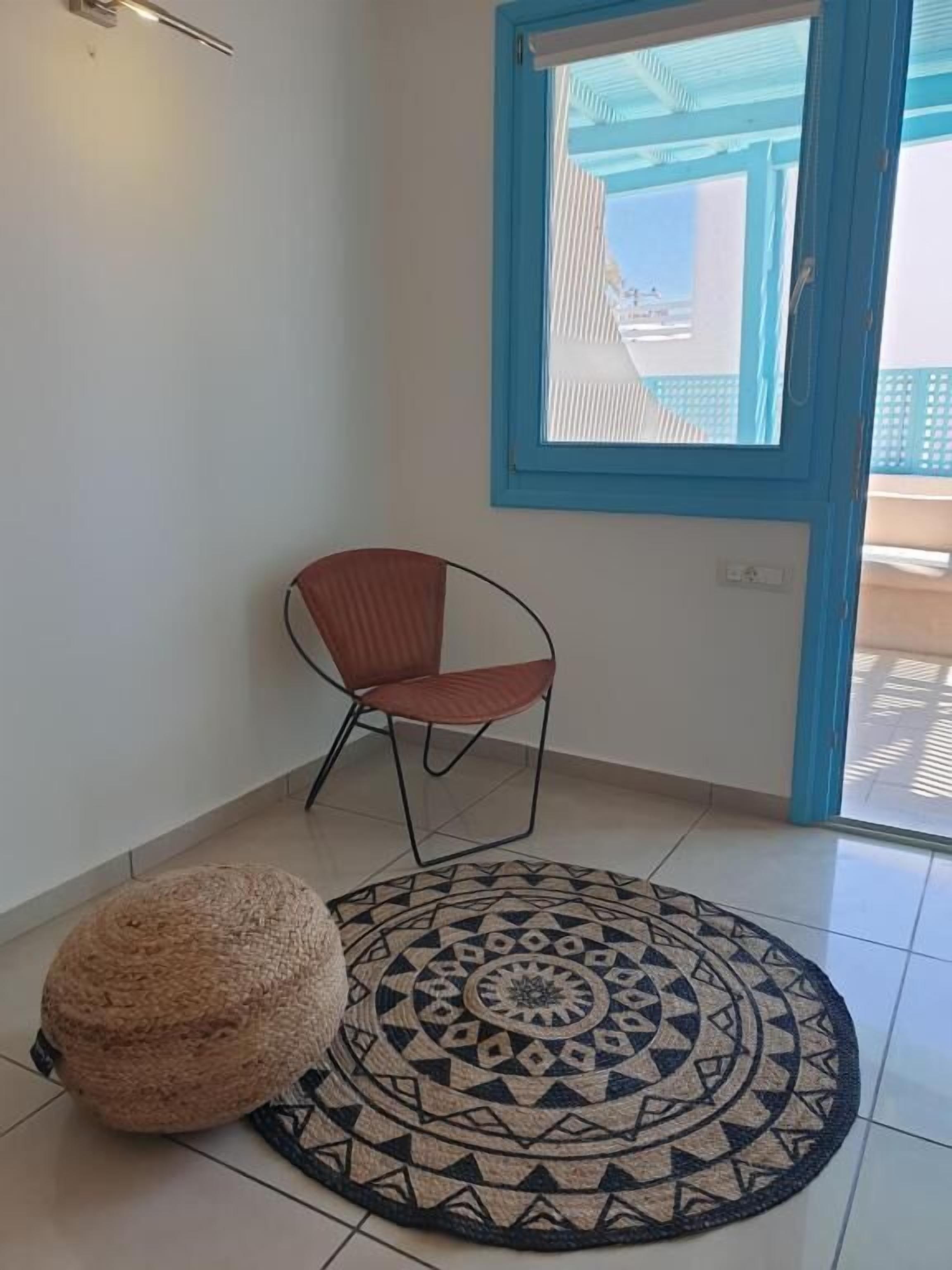 A room with a patterned rug, a single chair, and a small ottoman.