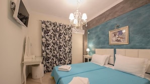 Une chambre à coucher comprenant un lit, un bureau, une chaise, un miroir, un lustre, un rideau et un tableau accroché au mur.