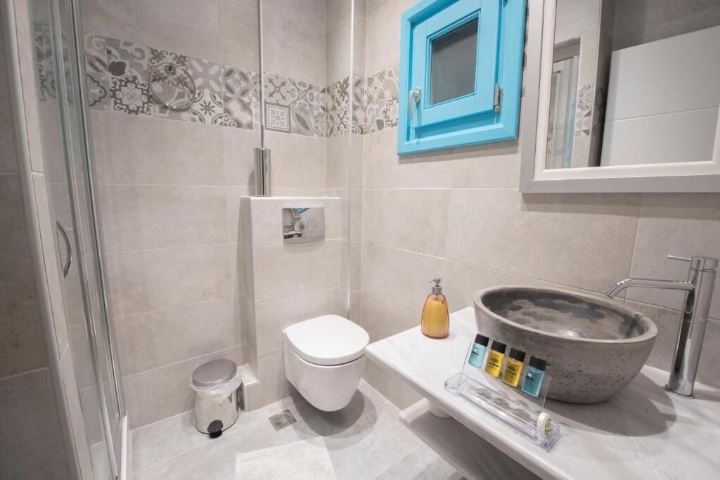 A bathroom with a shower, toilet, sink, and a blue-framed mirror.