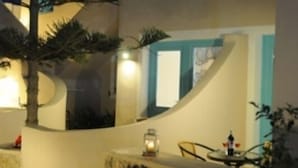 Un bâtiment moderne à l’extérieur blanc, agrémenté de touches de bleu, et doté d’un espace extérieur bien éclairé, avec des plantes et une table.