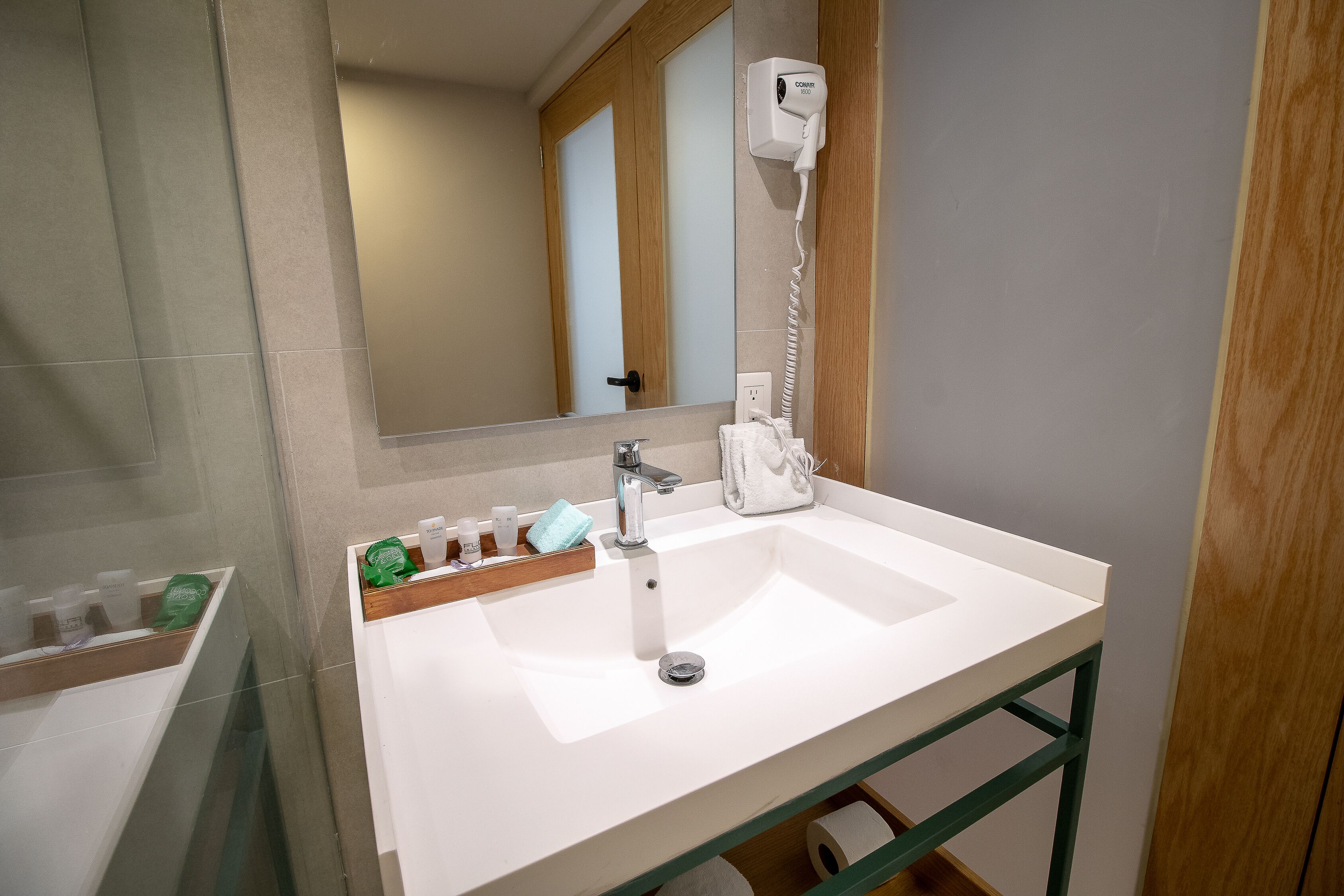 A bathroom with a white sink, a mirror, a hairdryer, and toiletries on the counter.