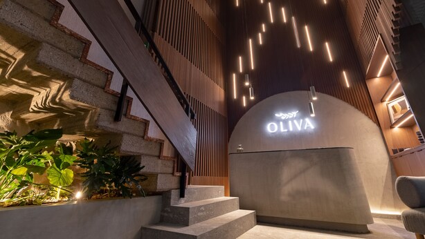 A reception area with a curved counter, a staircase with wooden railings, and a wall with vertical slats and hanging lights.