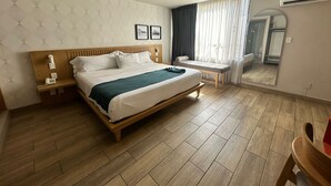 A hotel room with a wooden bed, bedside tables, a small desk, a mirror, and a window with curtains.
