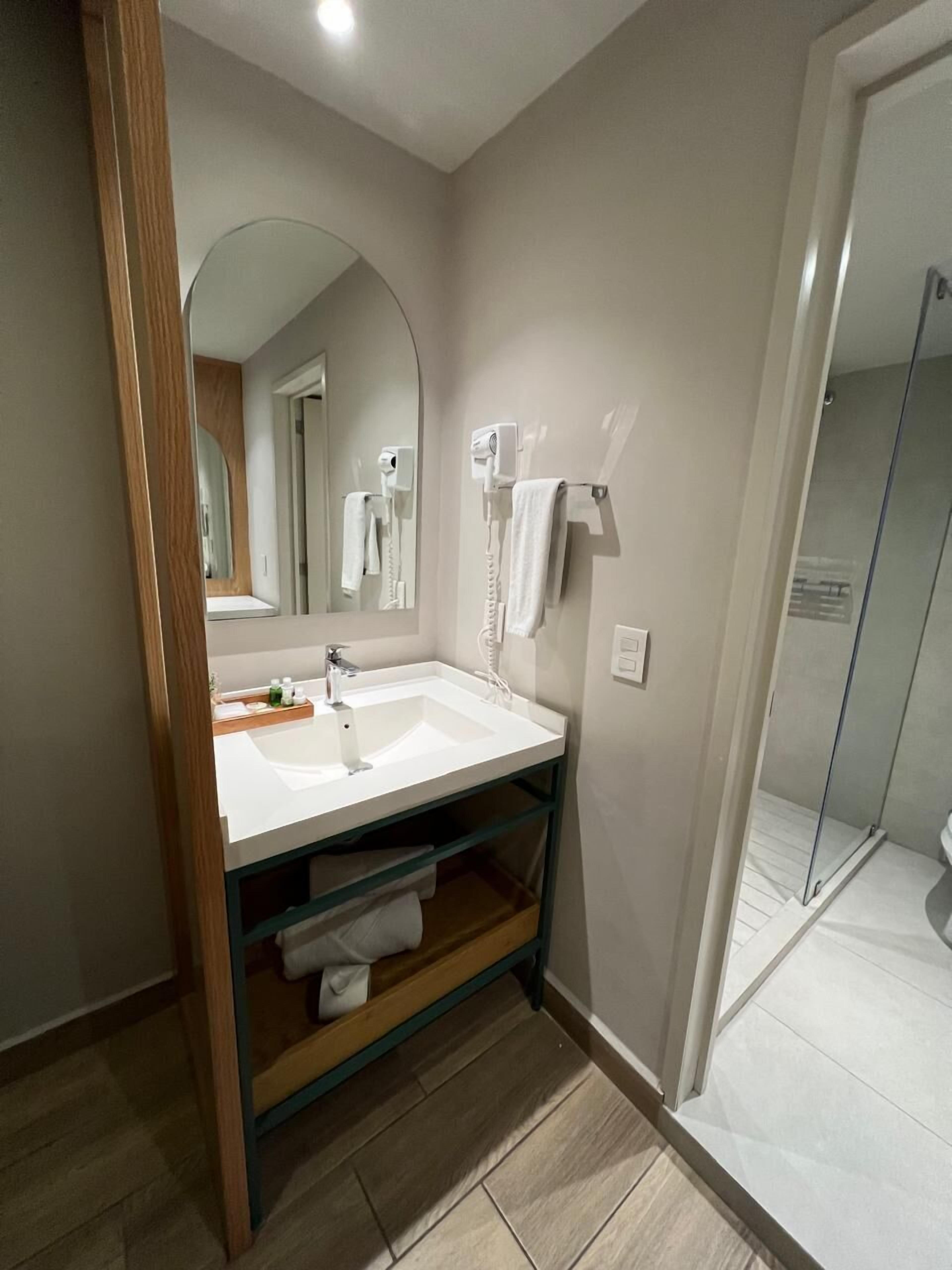 A modern bathroom with a white sink, a mirror, a towel rack, and a shower area.