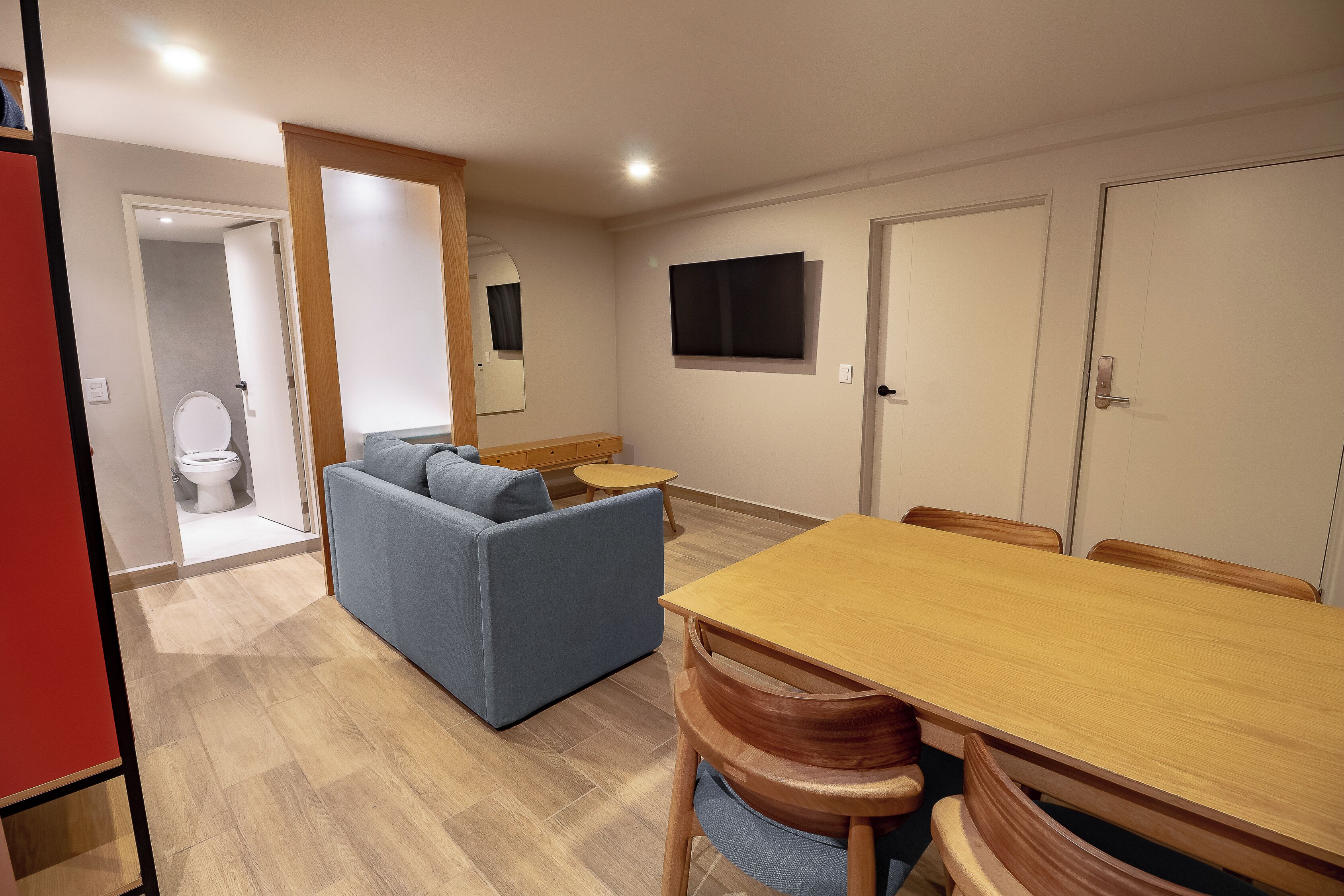 Una sala de estar moderna con un sofá, una mesa de comedor de madera y un televisor montado en la pared.