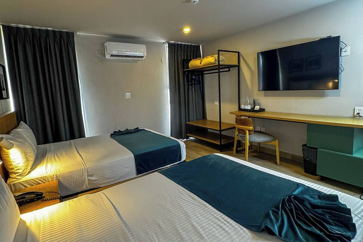 Habitación de hotel con dos camas, un escritorio, una silla, un televisor y un aire acondicionado.
