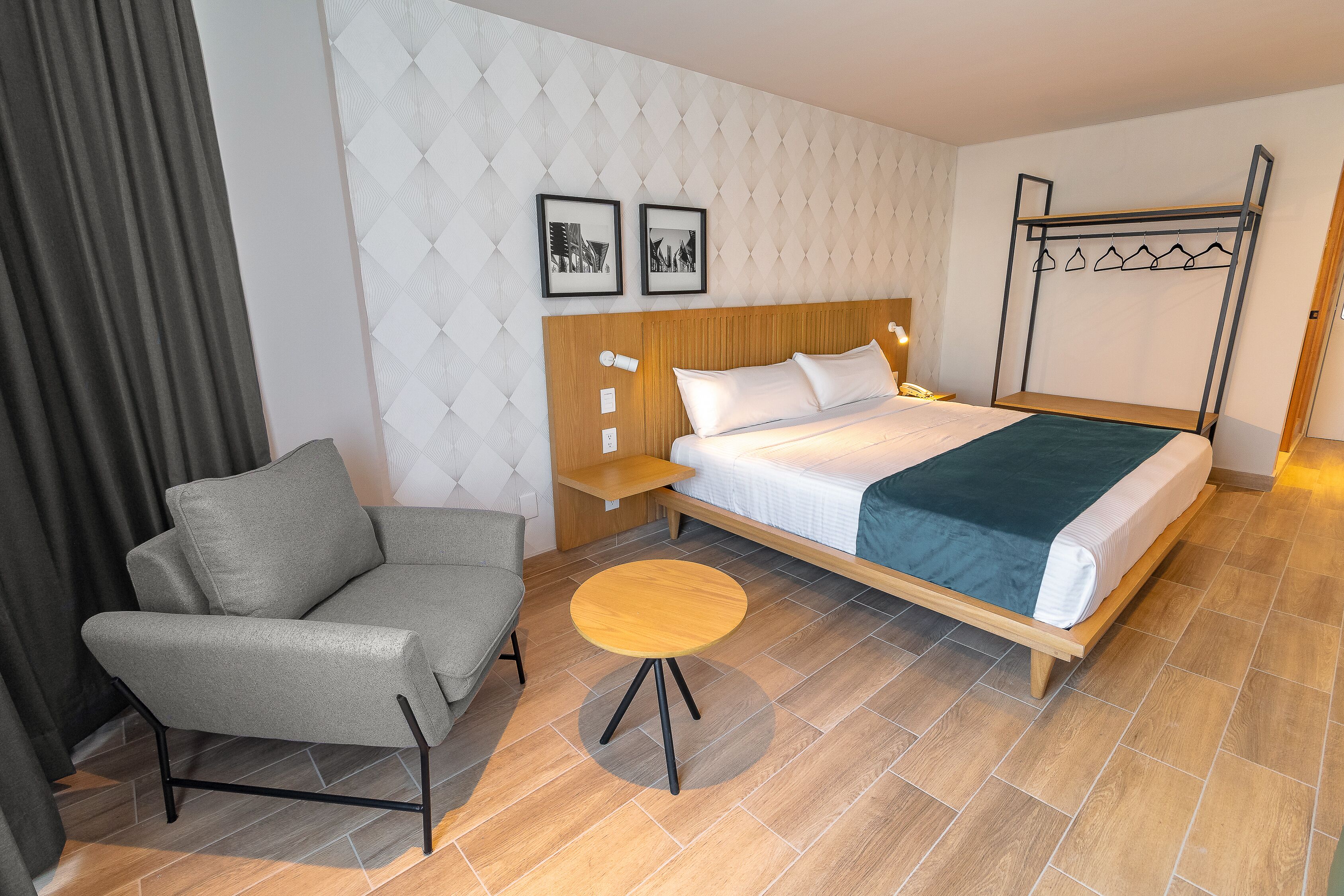 A hotel room with a bed, a grey sofa, a small round table, and a coat rack.