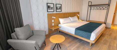 Una habitación de hotel con una cama, un sofá gris, una mesita redonda y un perchero.