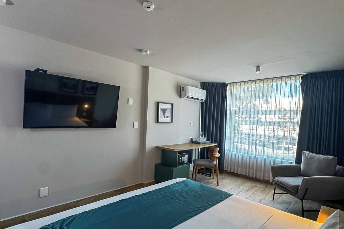 Habitación de hotel con cama, escritorio, silla, televisor y ventana con cortinas.