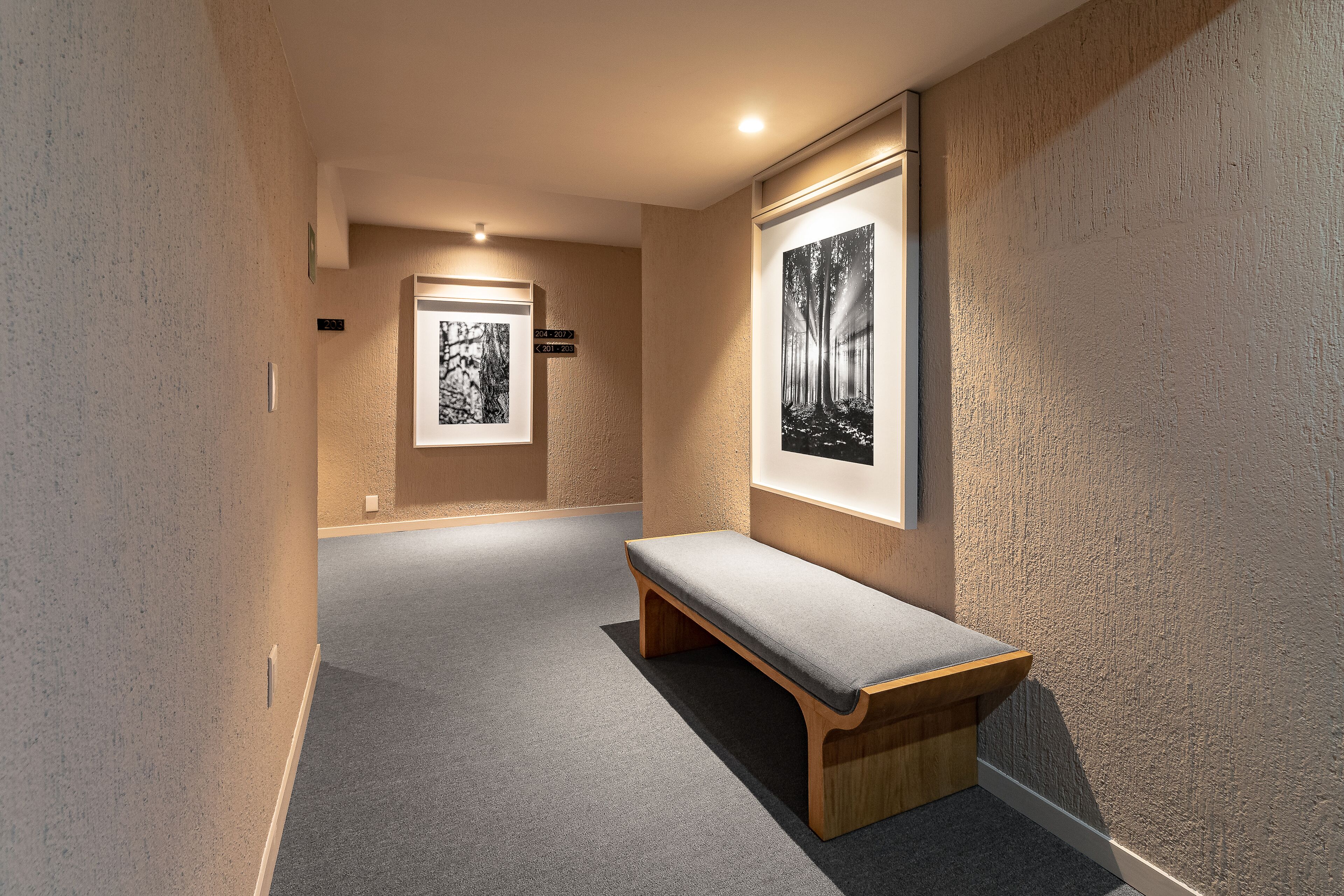 A hallway with a bench, framed artwork on the walls, and a carpeted floor.