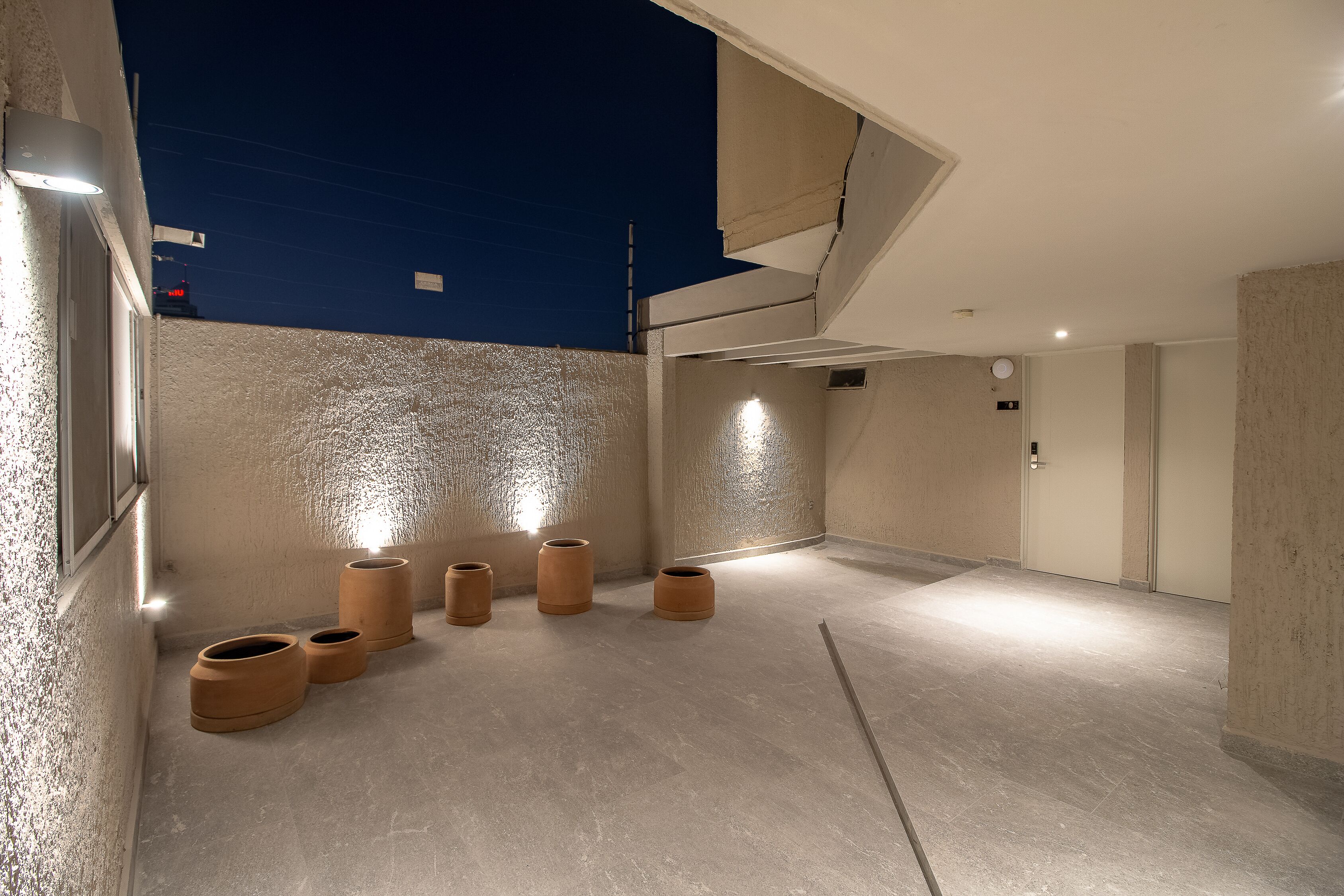 A modern, well-lit hallway with a concrete floor and walls, featuring several cylindrical objects and a visible door.