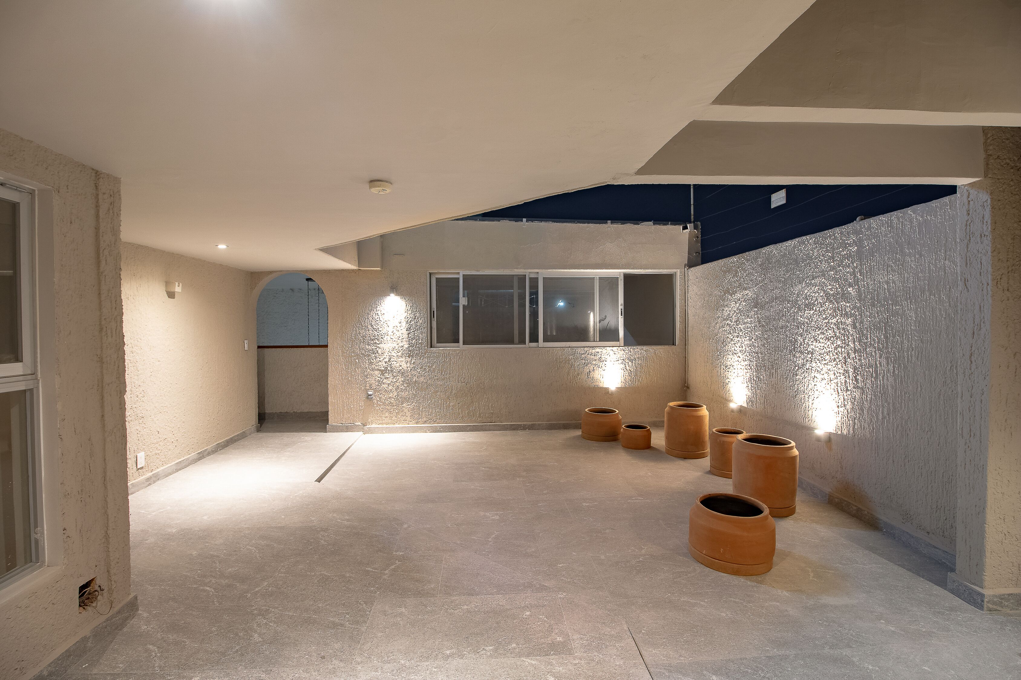 A spacious, well-lit interior with a high ceiling, large windows, and several terracotta planters.