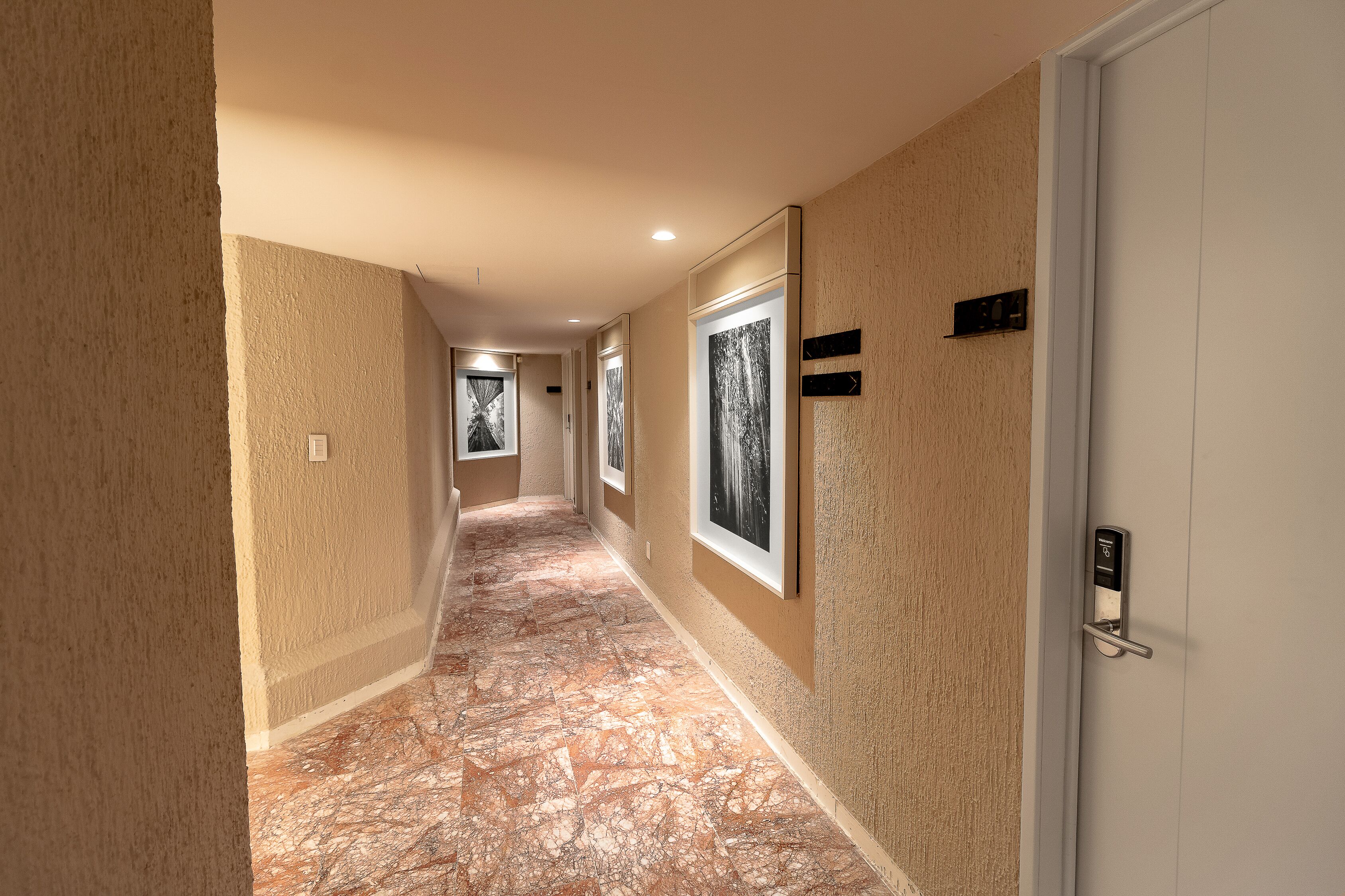 A hallway with a marble floor, beige walls, and framed pictures on the walls.
