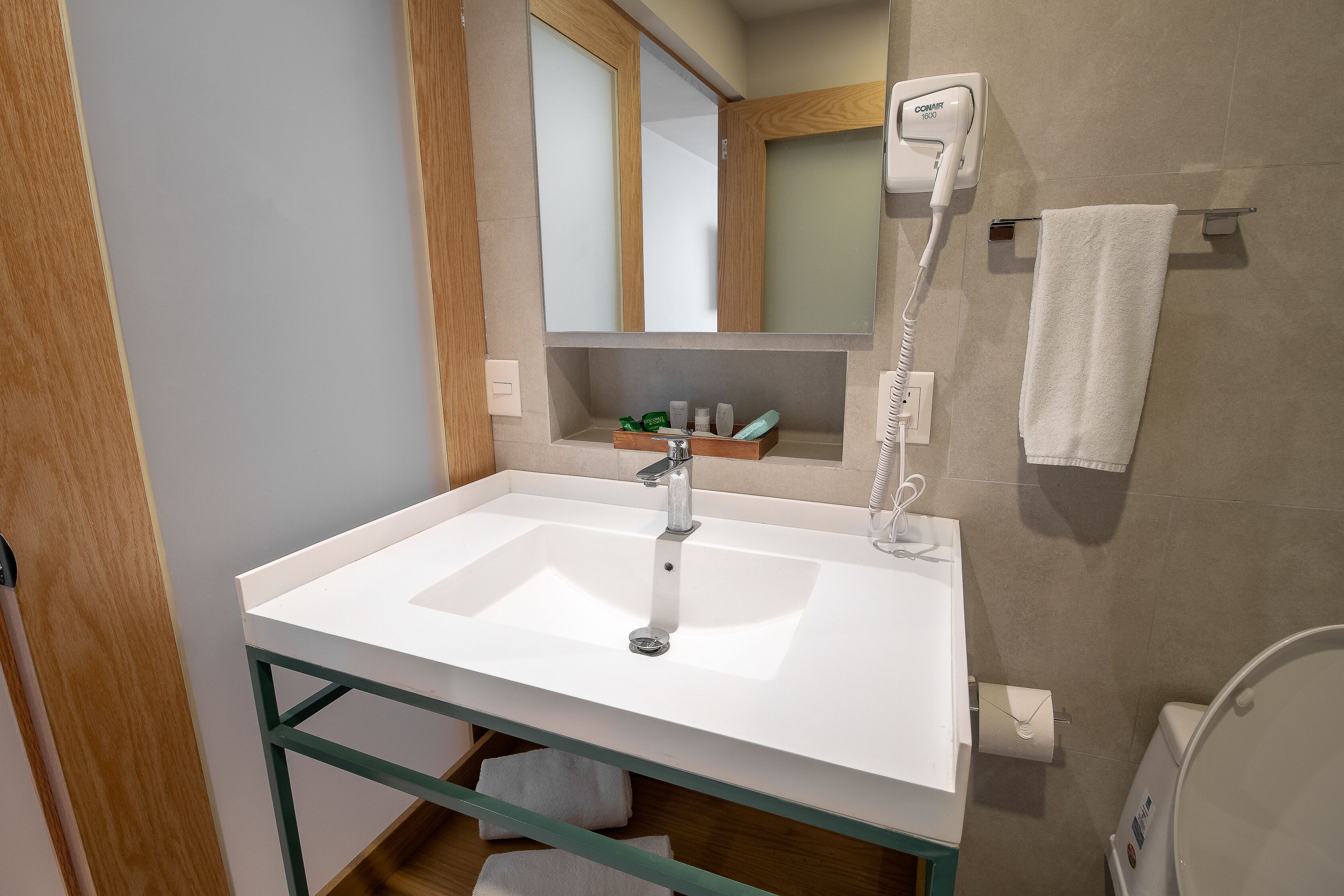 Un bagno con un lavandino bianco, uno specchio, un porta asciugamani e un asciugacapelli.