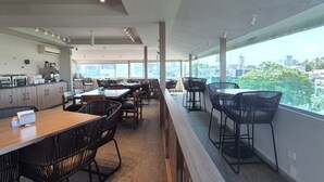 A modern dining area with high tables and chairs, a kitchen area with appliances, and large windows offering a city view.