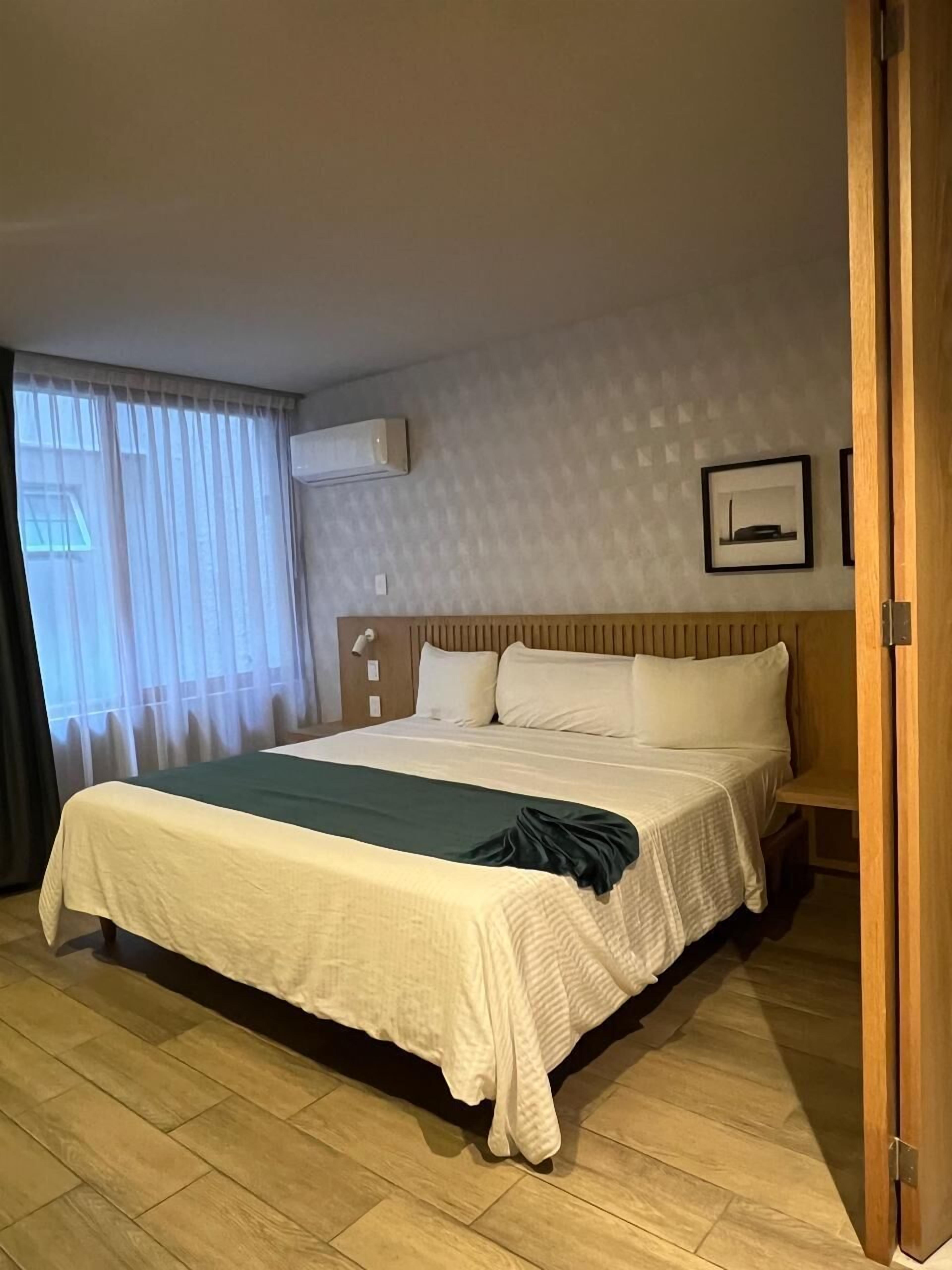 Une chambre d’hôtel avec un grand lit, un plancher en bois, un appareil de climatisation et une fenêtre avec des rideaux.