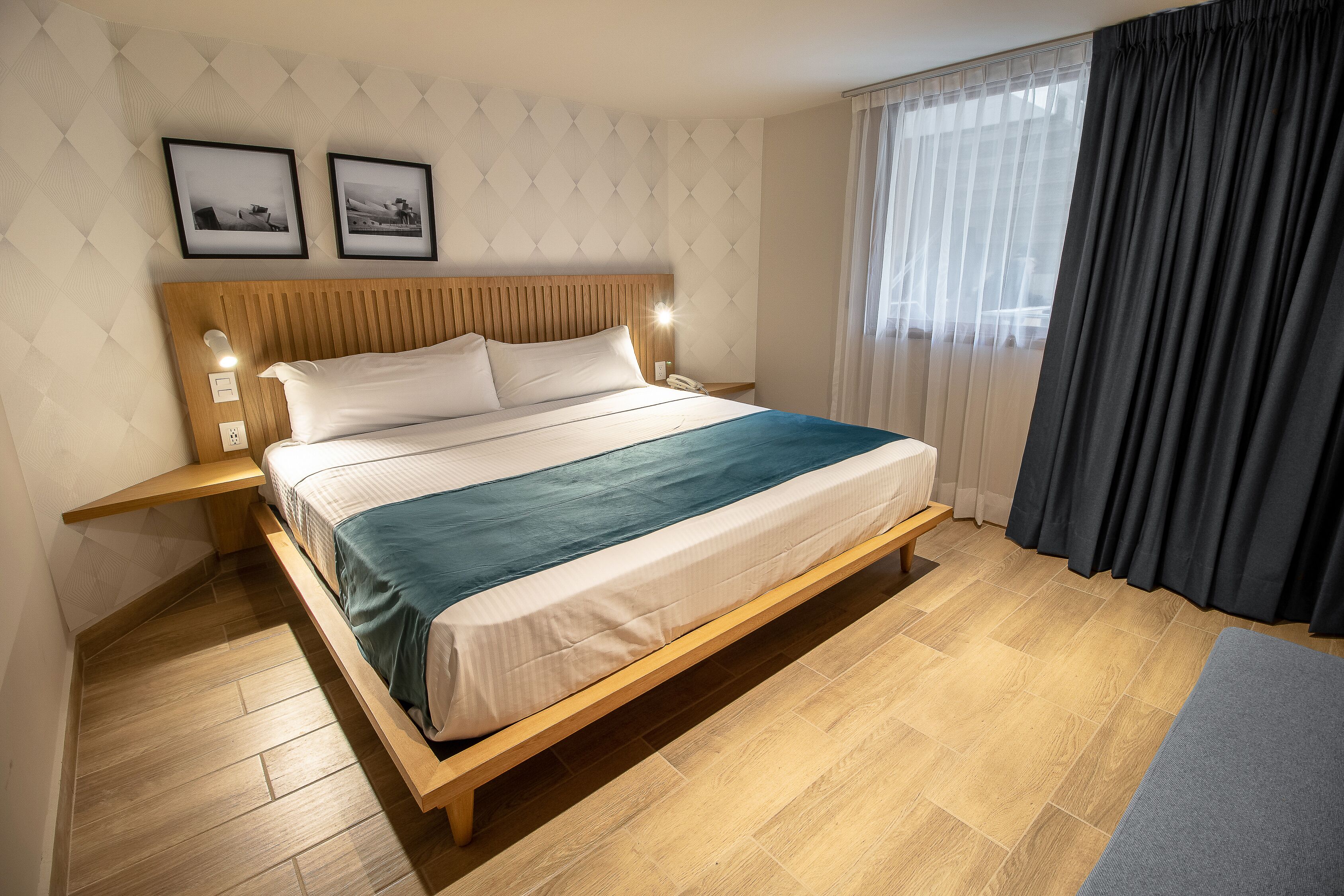 A modern bedroom with a wooden bed frame, a bedside table, and a nightstand. There are two framed pictures on the wall above the bed.