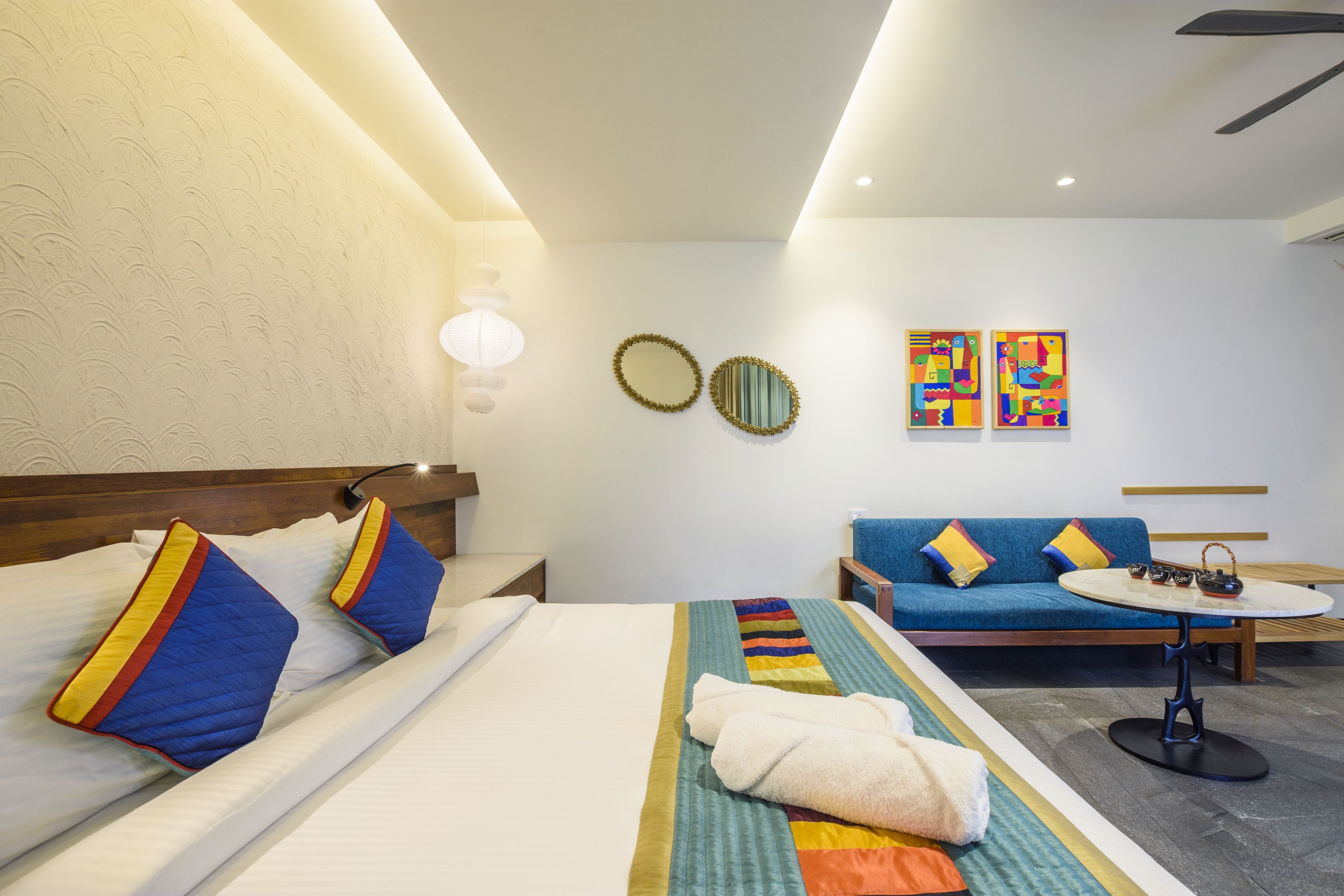 Una habitación de hotel con una cama, un sofá, una mesita y obras de arte en la pared.