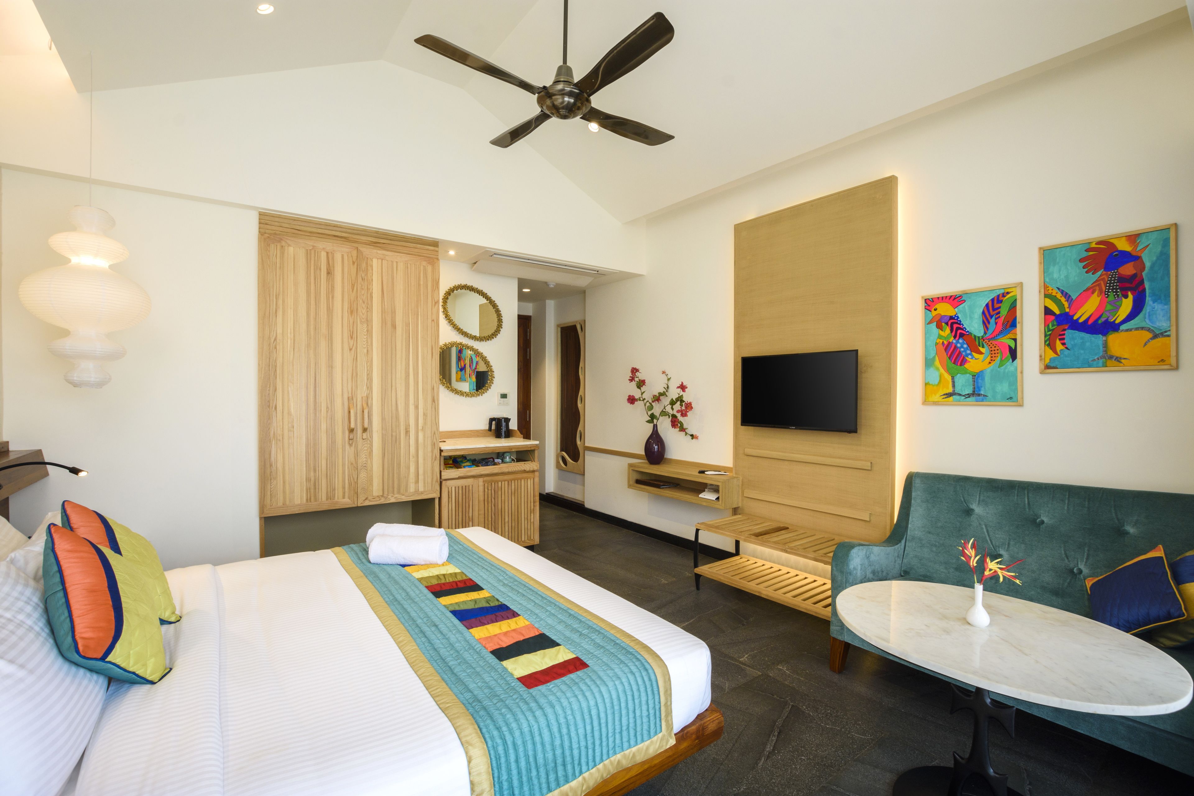A hotel room with a bed, a green sofa, a small table, a TV, and artwork on the walls.