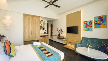 A hotel room with a bed, a green sofa, a small table, a TV, and artwork on the walls.