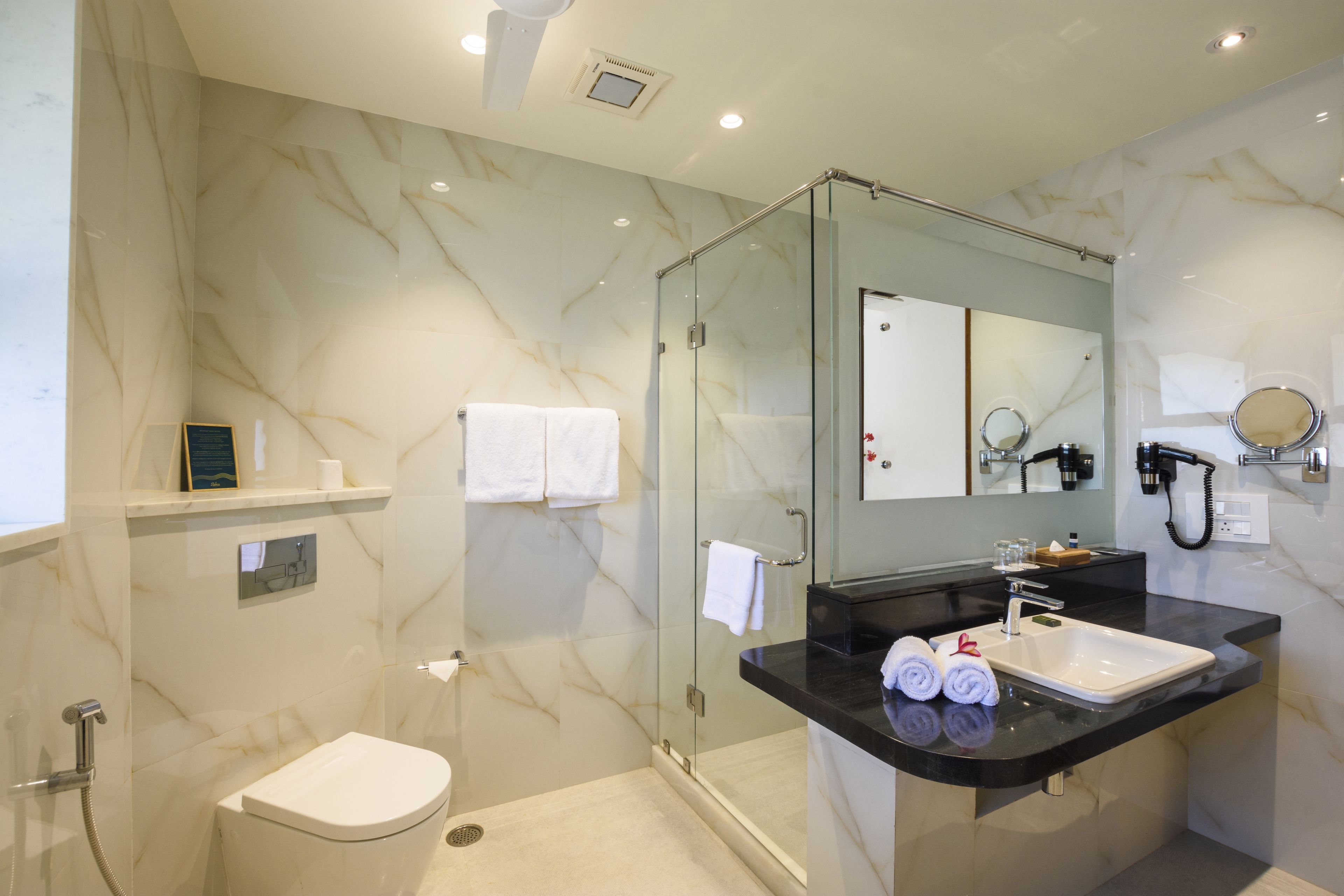 A modern bathroom with a glass shower enclosure, a white toilet, a black sink with a mirror above it, and a towel rack with two towels.