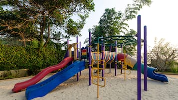 Explore the playground with slides and climbing frames set amidst lush greenery and trees.