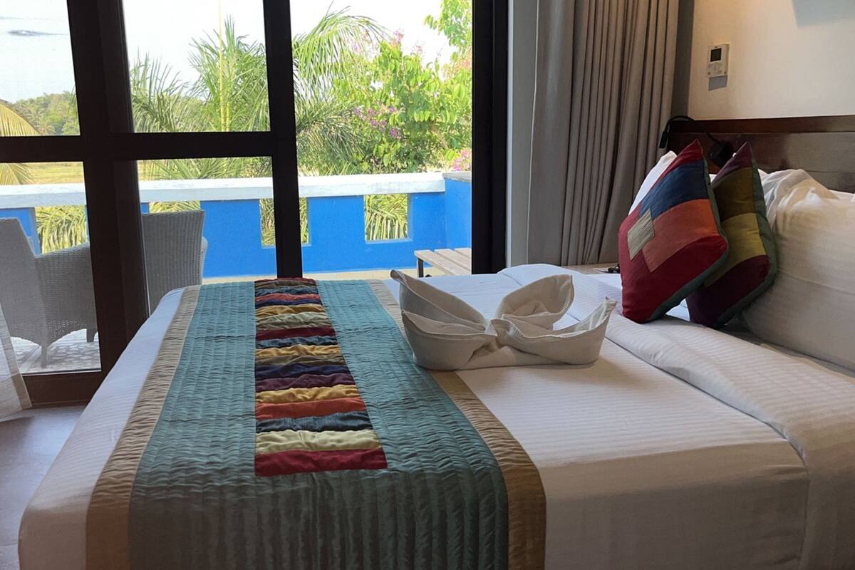 A hotel room with a bed, a view of the outdoors, and a window with curtains.