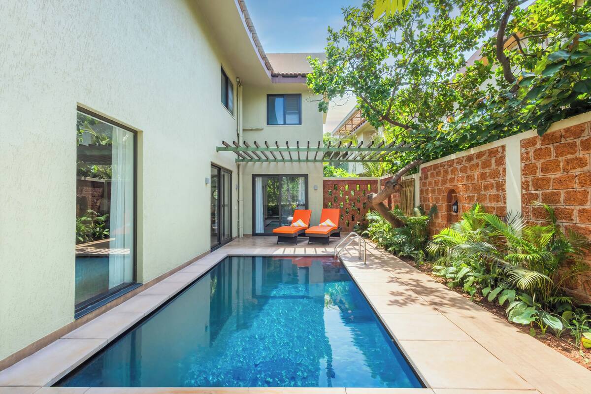 A swimming pool with two orange lounge chairs, a pergola, and a brick wall with plants.
