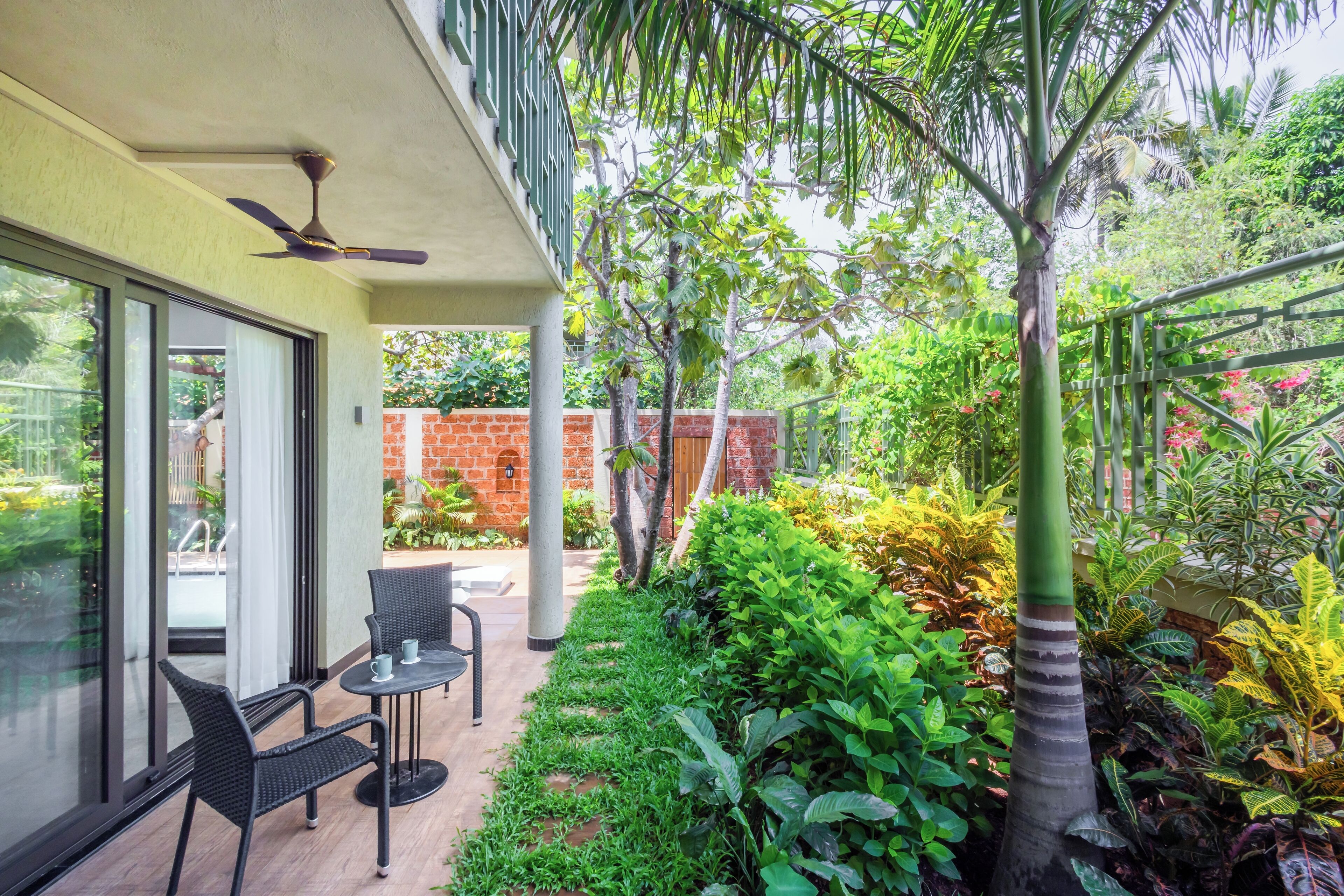 A patio with a table and chairs, surrounded by lush greenery and a brick wall.