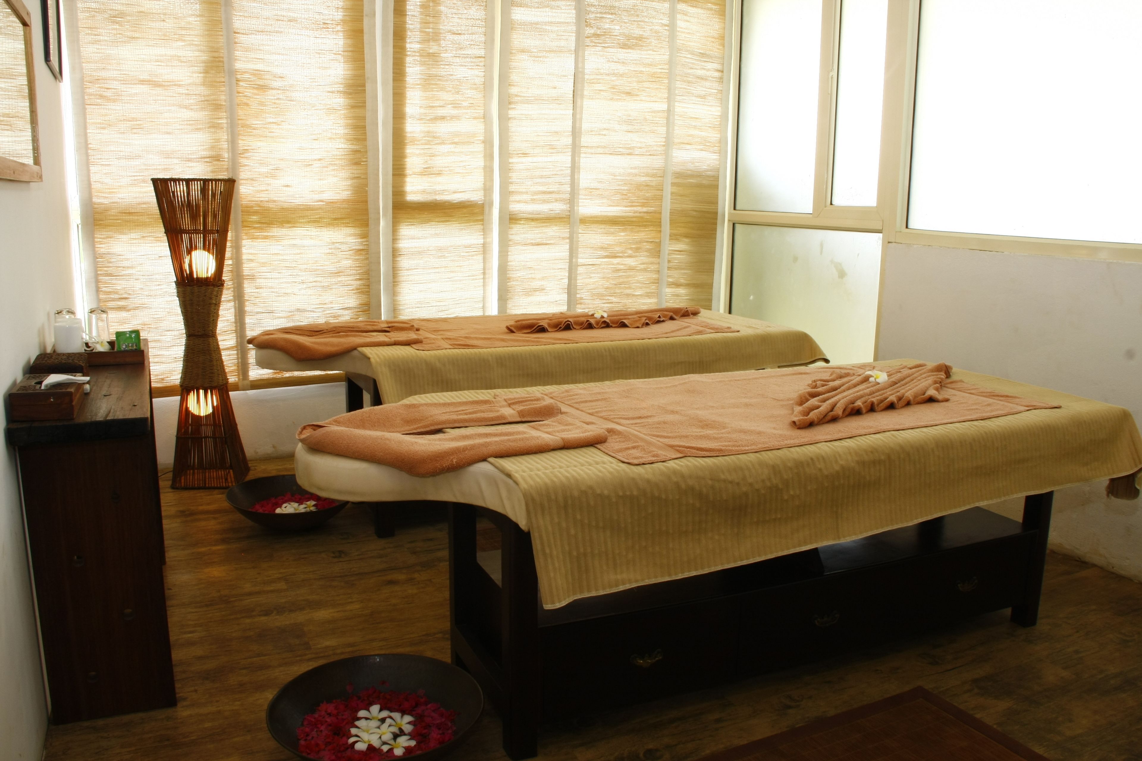 A room with two massage tables, a wooden floor, and a large window with vertical blinds.