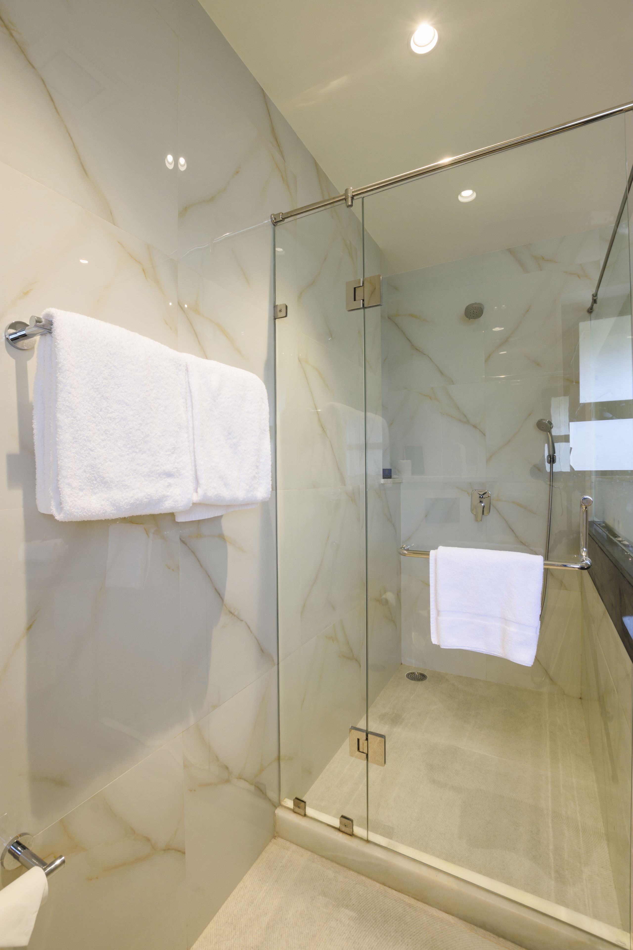 A modern bathroom with a glass-enclosed shower, marble walls, and white towels.