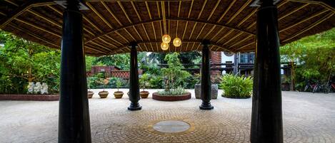 Un espacio al aire libre techado con suelo de baldosas, columnas e iluminación colgante.