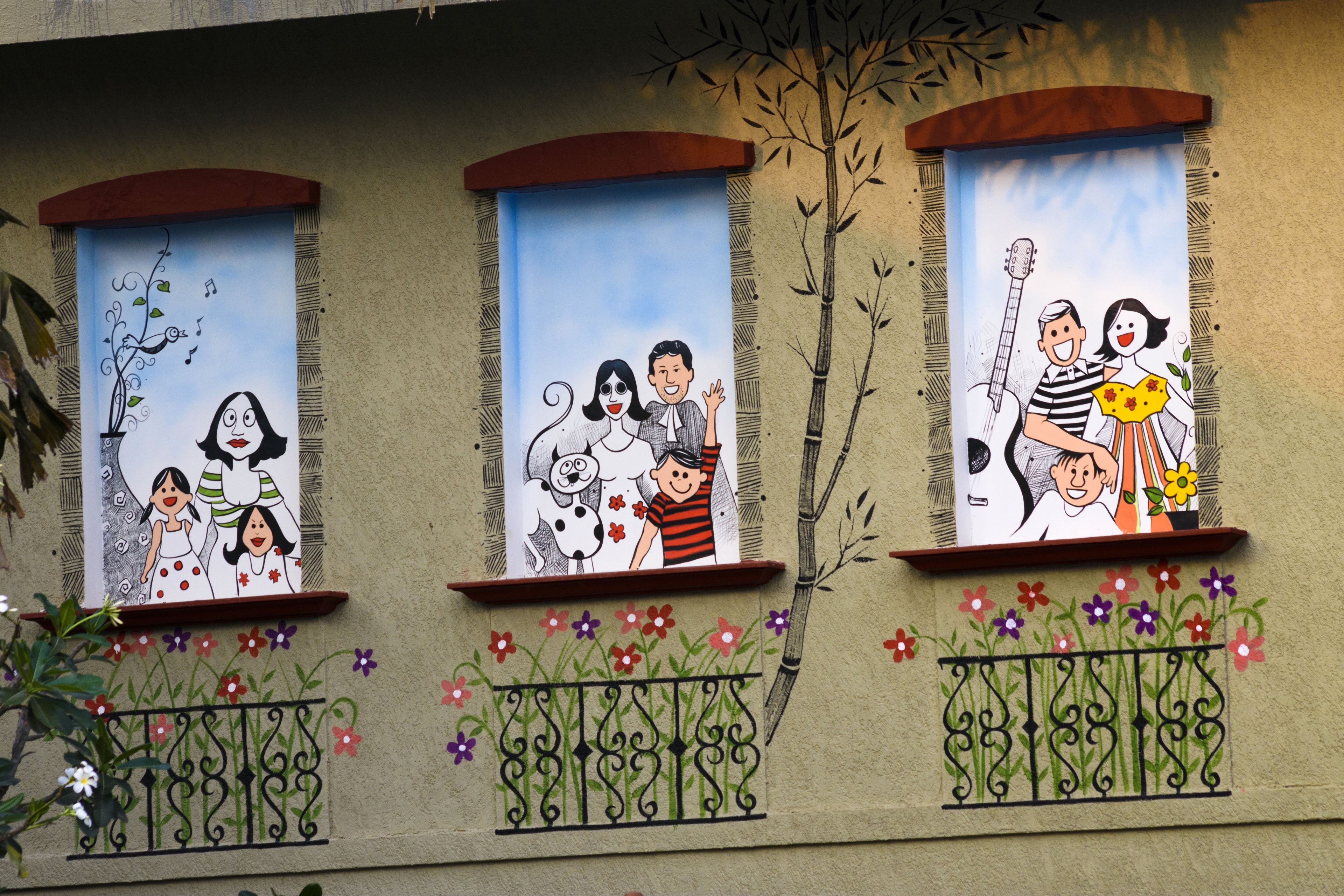 Fachada de edificio con tres ventanas, cada una decorada con murales coloridos que muestran familias y niños.